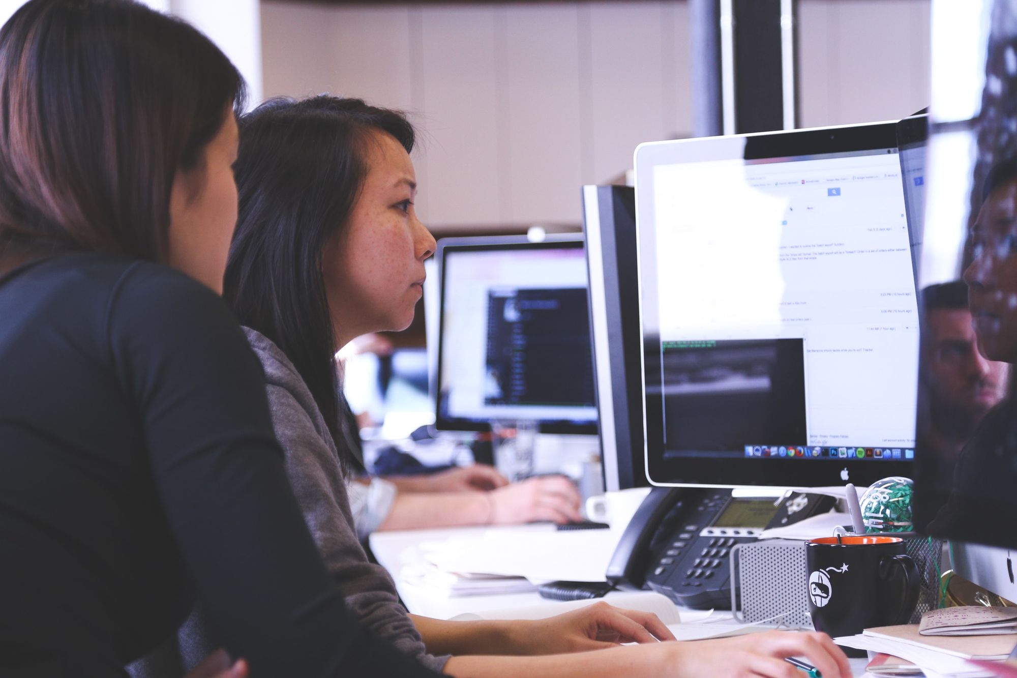 Two women sitting in front of a computer screen 